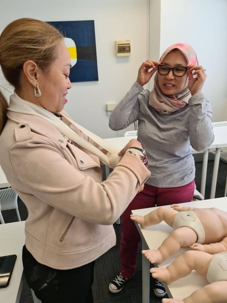 Two candidates practising arm sling bandaging together during face-to-face First Aid training