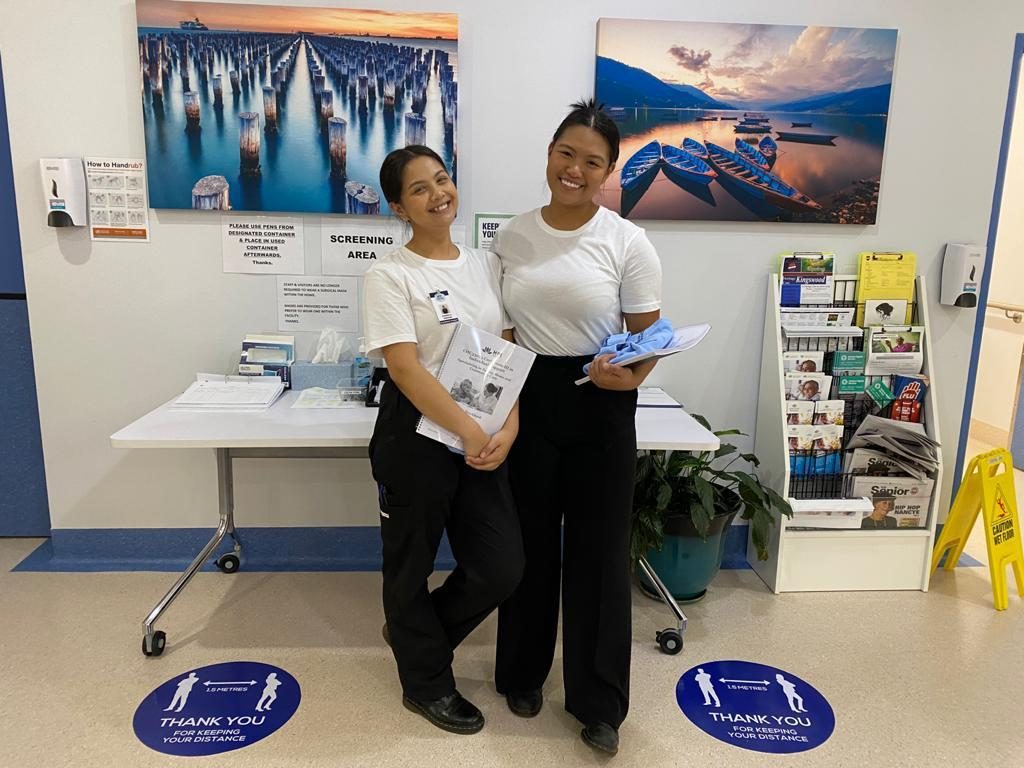 Two smiling candidates in uniform holding their training logbooks at their OJT placement facility