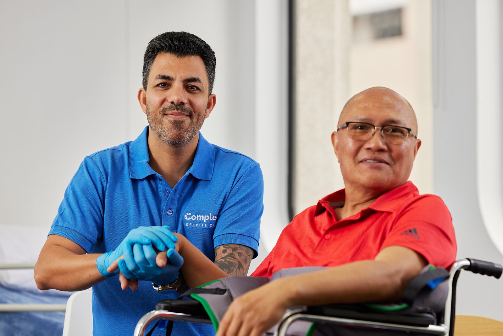 A support worker warmly holding hands with a client, both smiling to camera